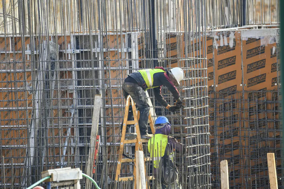 Handwerker auf einer Leiter an einem Rohbau mit Bewehrungsstahl
